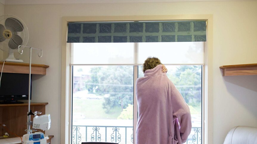 Sue Jensen stares out the window in dressing gown.