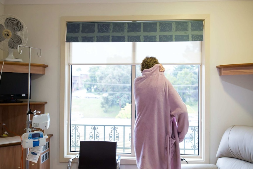 Sue Jensen stares out the window in dressing gown.