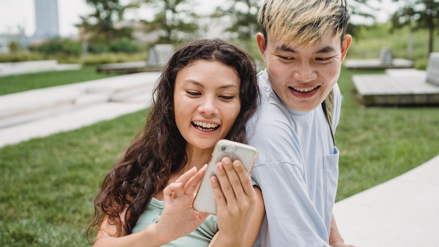 A young man and woman look at a phone and laugh.