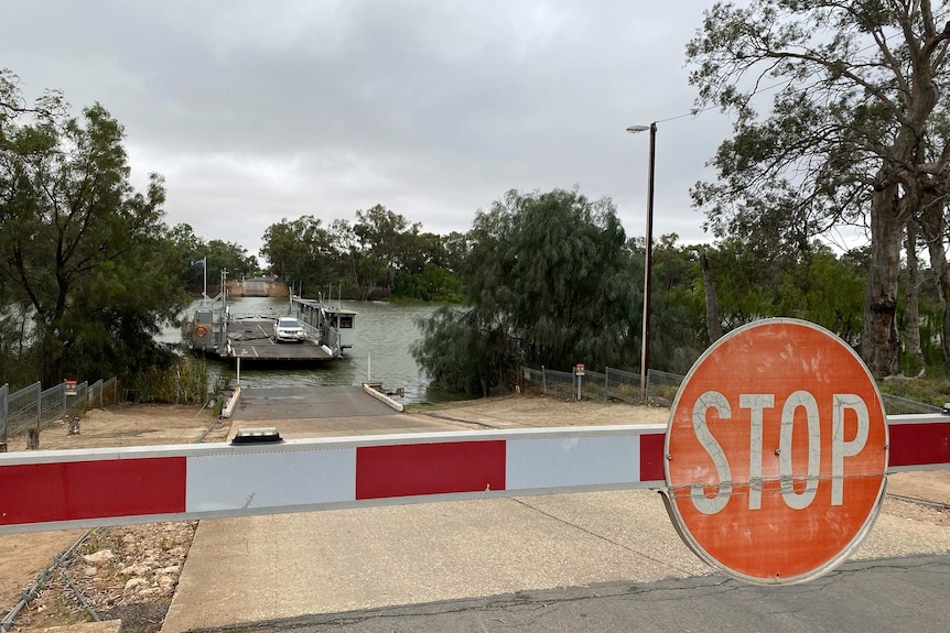 A car transportation ferry in the background pulls into a ramp on the Murray River while a stop sign sits in the foreground