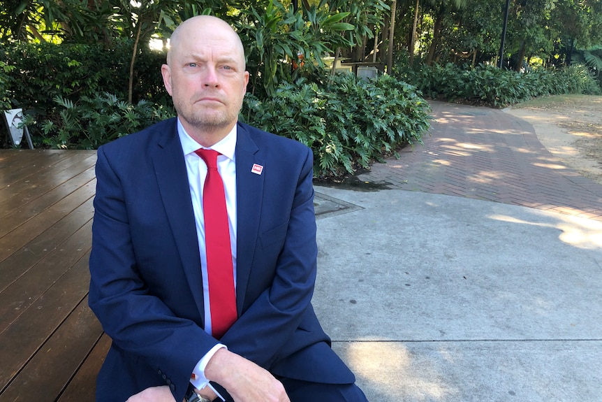 des in a suit with greenery behind him in a park