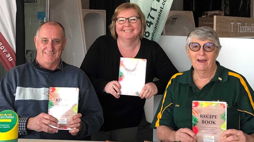 A man and two woman behind a table each holding a recipe book