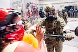 A federal officer uses a baton to push back demonstrators from a building covered in graffiti.