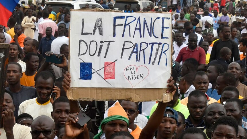 A large crowd of Nigerien men - one holding a sign saying "France Must Leave"