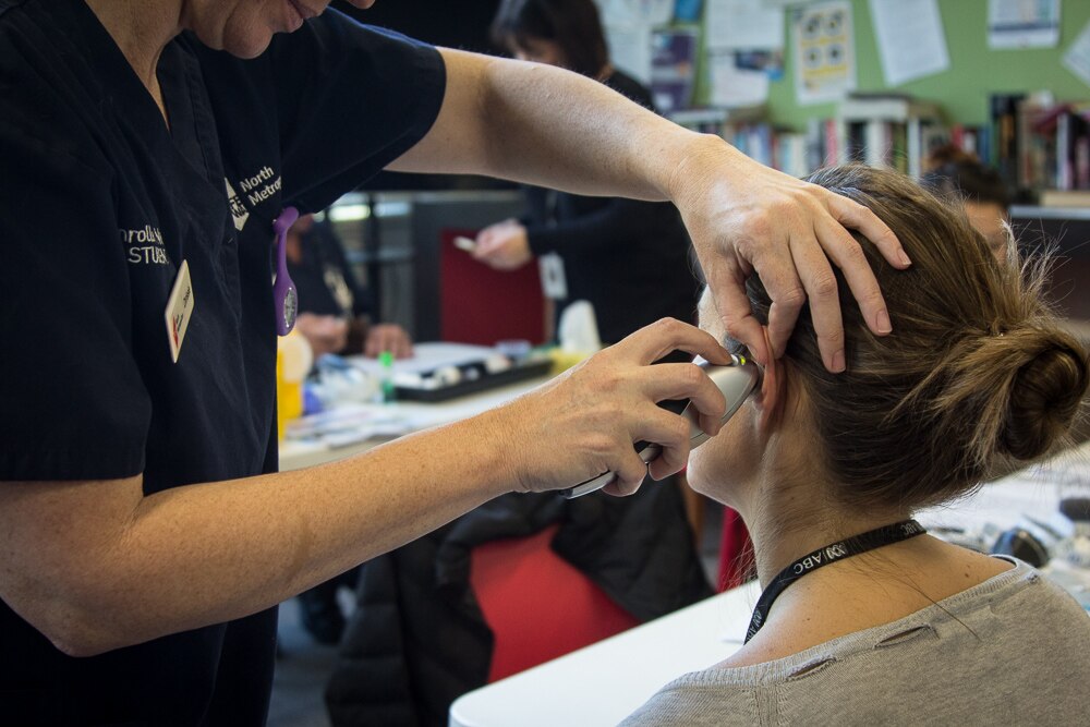 A faceless person takes the temperature of a patient using an ear thermometer in a hospital