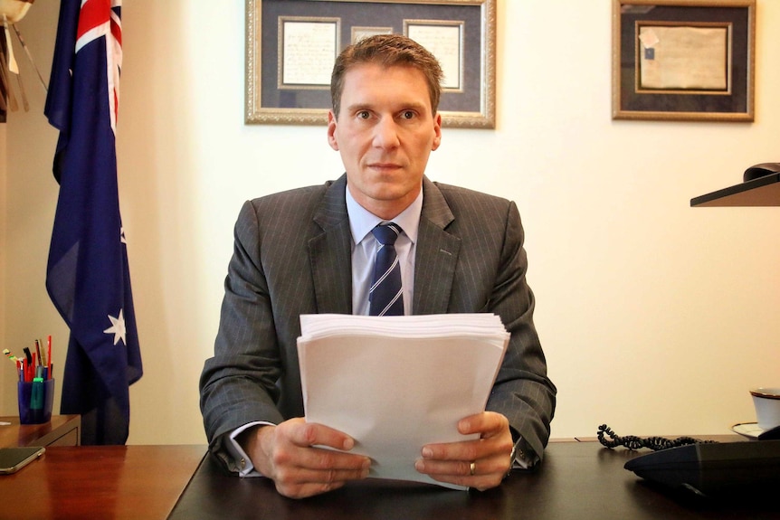 Cory Bernardi sits as his desk in his office in Parliament House, Canberra, holding A4 sheets of paper in his hands.