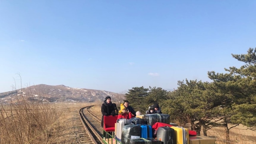 Several people stand behind luggage on a hand-propelled rail car