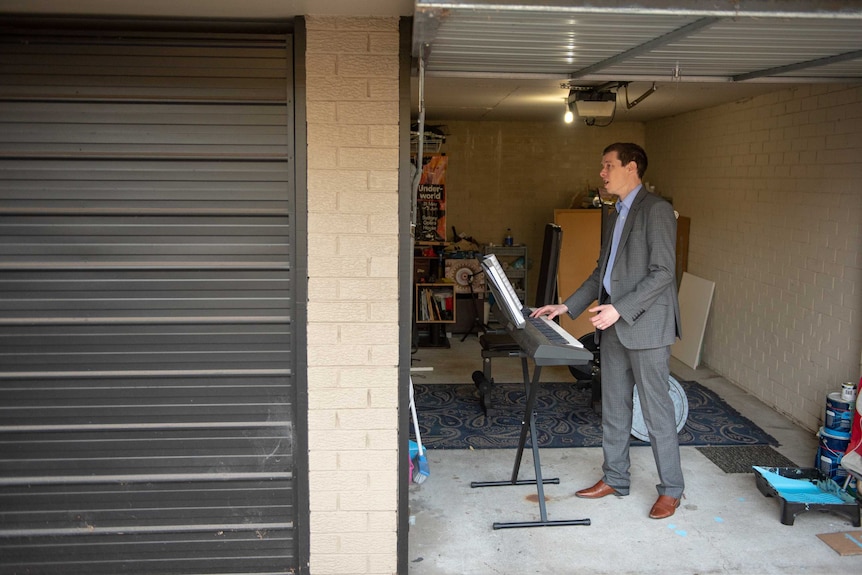 A man stands in the garage of his Sydney apartment, singing and playing a keyboard.