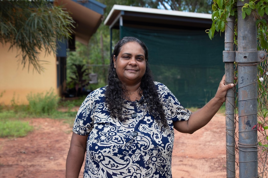 A woman stands outside her house.