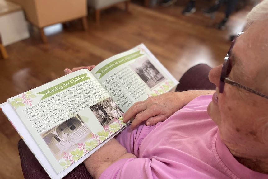 An older woman looks over a book of her memoirs, showing old photos and writing.