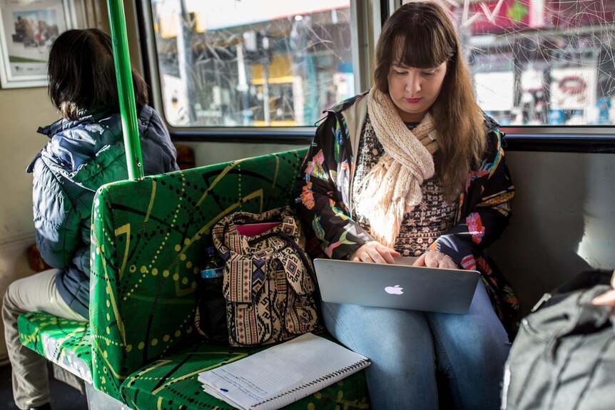 Shannon Colee balances a computer on her lap while travelling on a tram to university.