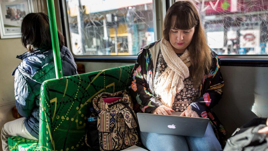 Shannon Colee balances a computer on her lap while travelling on a tram to university.