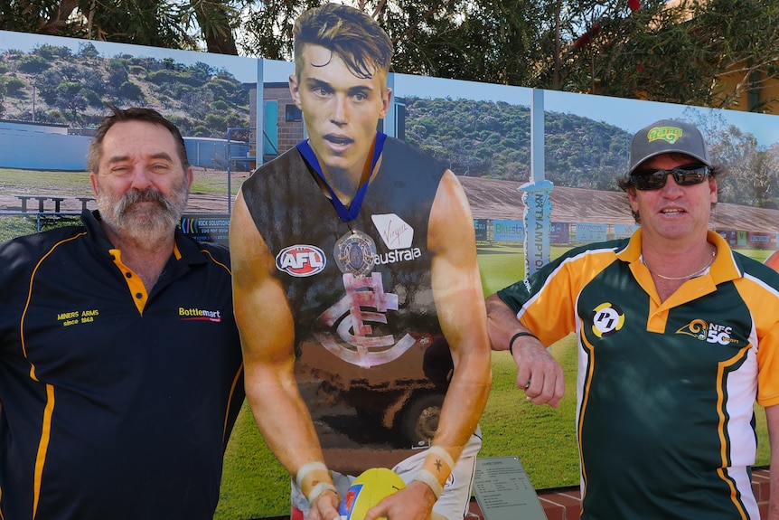 Two men stand next to a statue of an AFL player