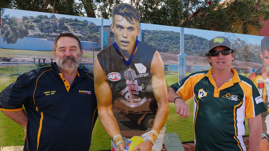 Two men stand next to a statue of an AFL player