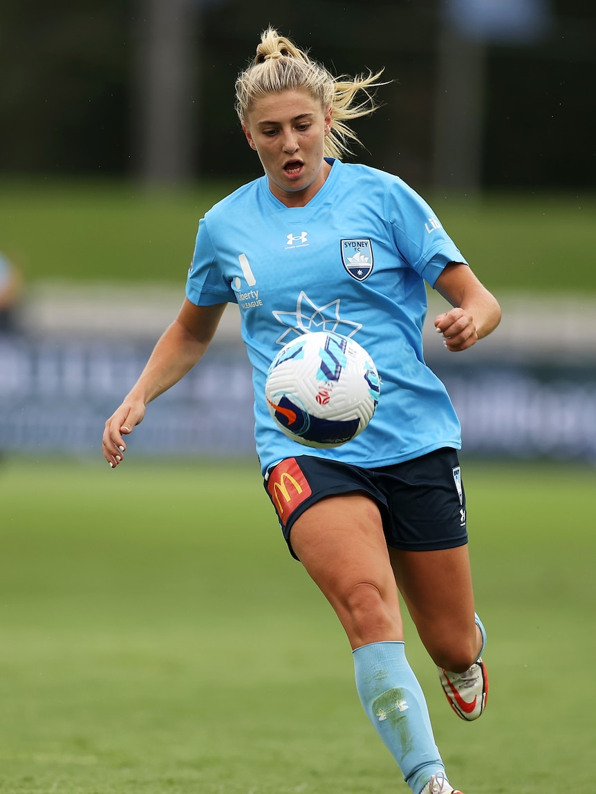 A soccer player wearing sky blue looks at a ball during a game