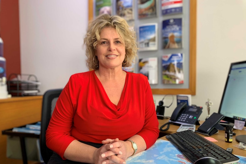 Joanne Harding-Smith sits behind a desk with a map and travel brochures in the background.