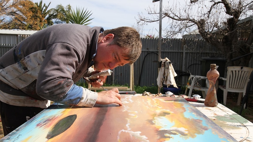 A male artist concentrates on painting in his open air studio