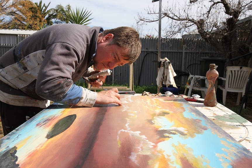A male artist concentrates on painting in his open air studio