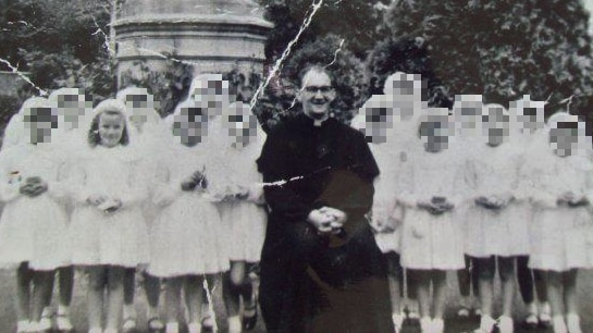 A group of young girls in their communion dresses with a Chaplain sitting in his robes in the middle of the group