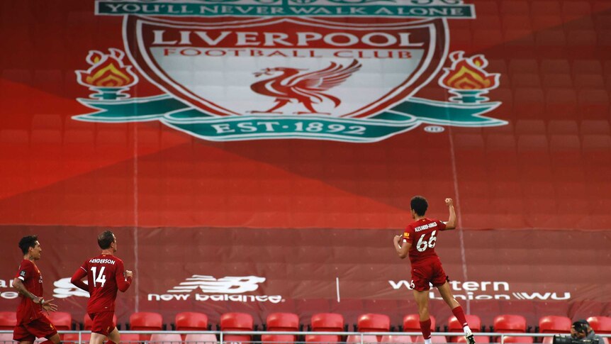 A footballer leaps in the air after scoring, with a huge Liverpool logo visible in the background.