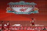 A footballer leaps in the air after scoring, with a huge Liverpool logo visible in the background.