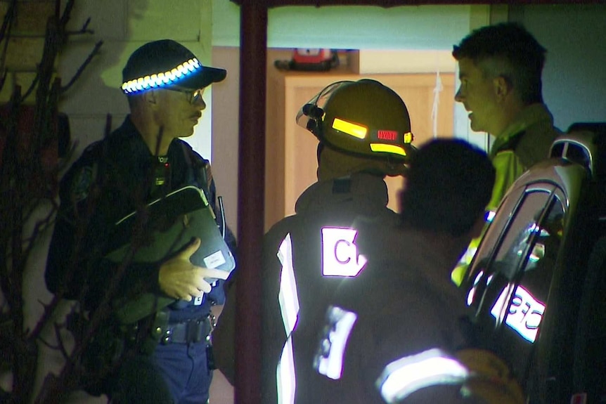 A police officer standing next to two CFS officers wearing yellow overalls