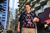 Disability advocate Brendon Donohue stands in front of a high rise with his cane.