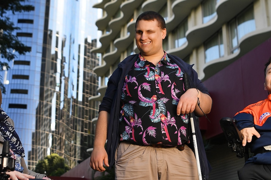 Disability advocate Brendon Donohue stands in front of a high rise with his cane.