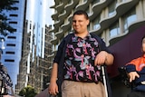 Disability advocate Brendon Donohue stands in front of a high rise with his cane.