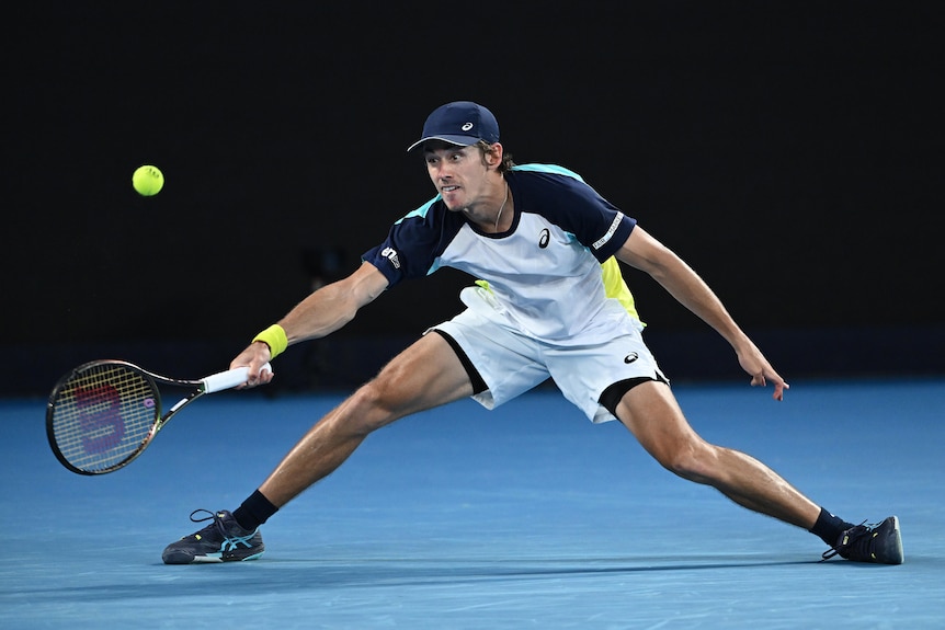 An Australian male tennis player stretches to his right to make a forehand return.
