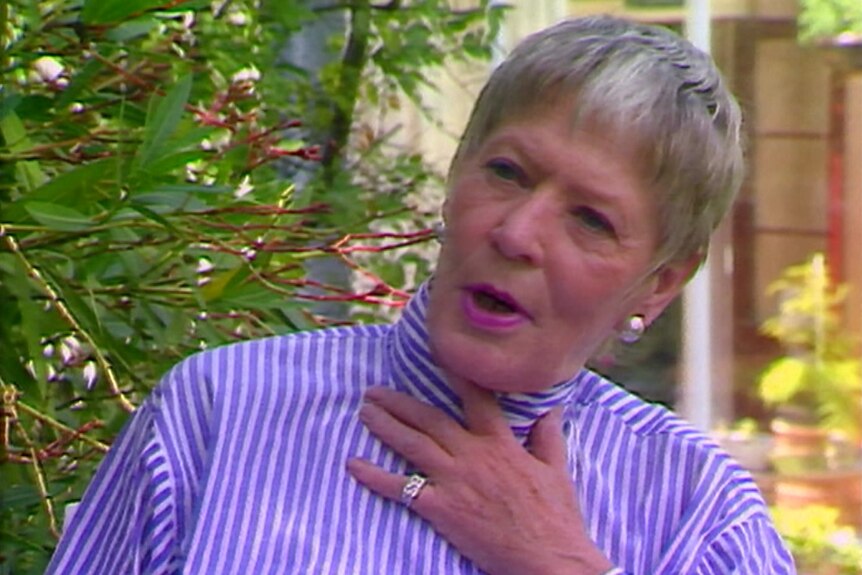 a woman in a purple shirt and lip stick, her hand is on her chest