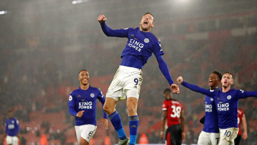 Leicester City's Jamie Vardy leaps in the air in jubilation, eyes closed, fist clenched. His teammates are nearby.