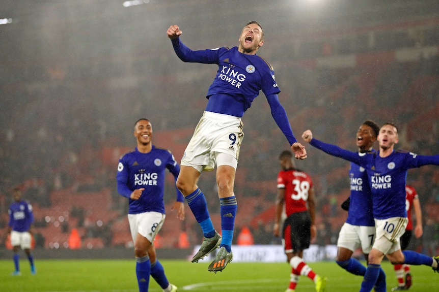 Leicester City's Jamie Vardy leaps in the air in jubilation, eyes closed, fist clenched. His teammates are nearby.