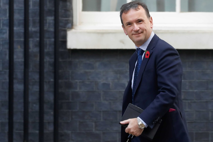 Alun Cairns wears a suit as he walks along looking at the camera