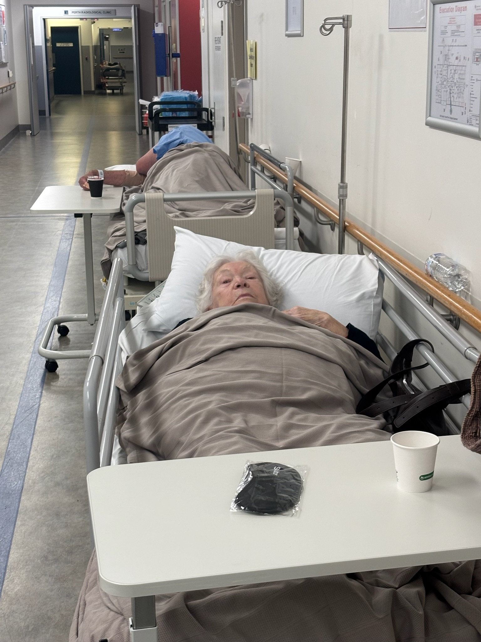 A elderly person lies in a bed at a hospital corridor. 
