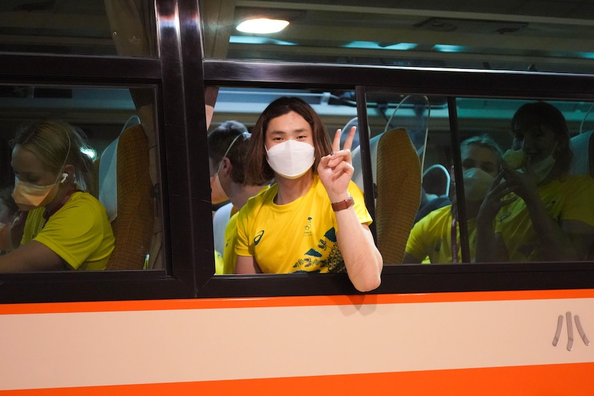 A young man in a yellow jersey and white face mask gives a peace sign out 