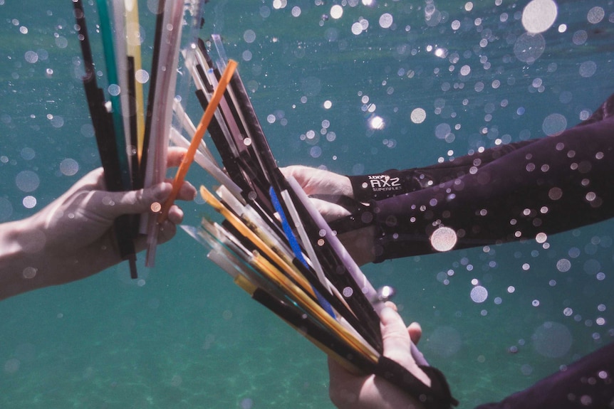 Underwater photo of hands holding big bunches of plastic straws.