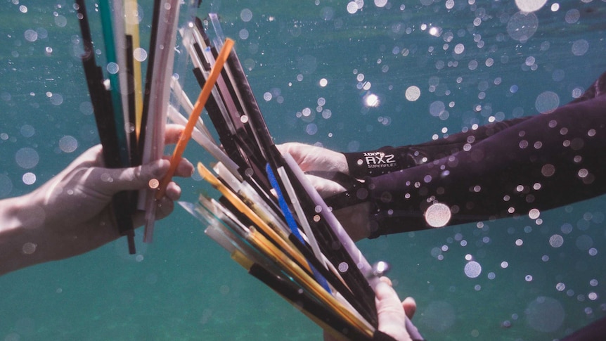 Underwater photo of hands holding big bunches of plastic straws.