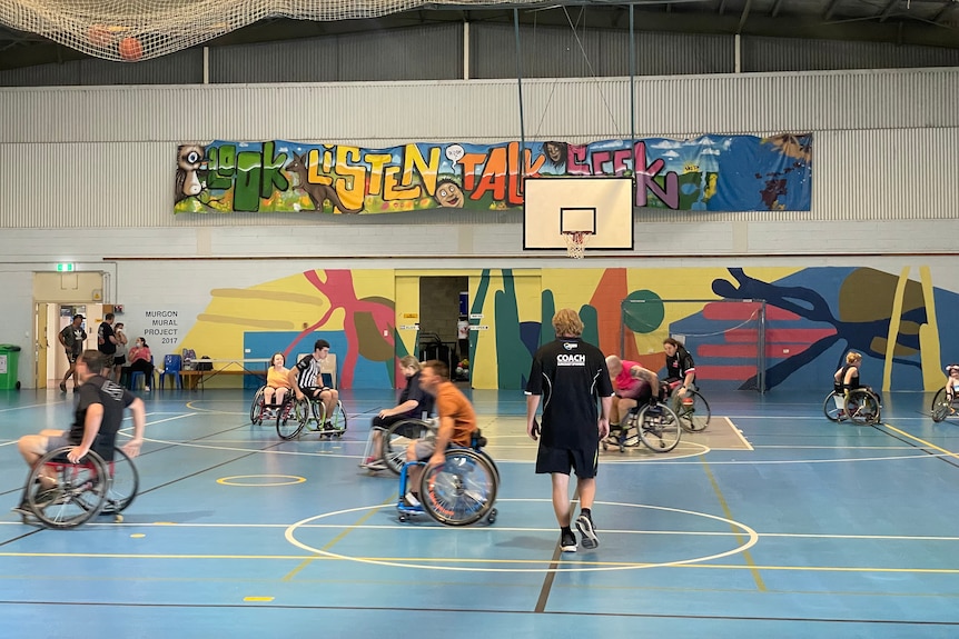 A group of people play wheelchair basketball on a colourful indoor court