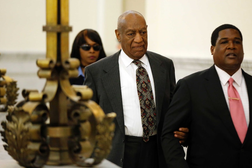 Bill Cosby leaves court holding a member of his entourage.