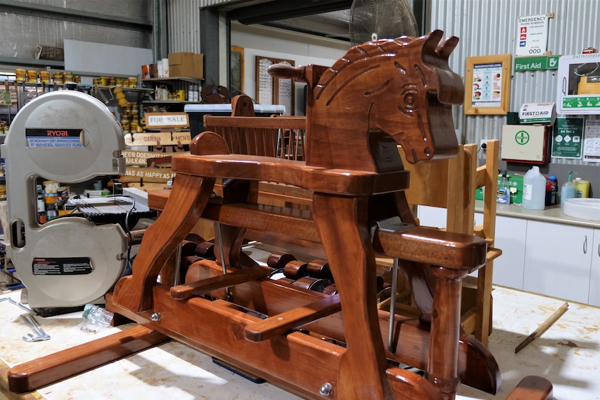 A solid timber rocking horse is displayed on a table. 