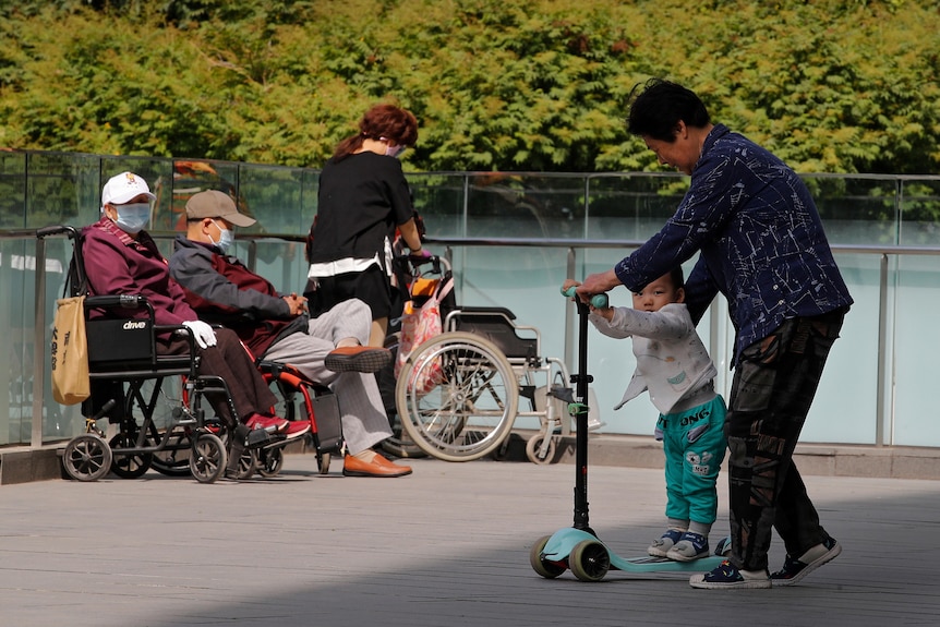 Une femme et un enfant sur un scooter avec des personnes âgées en arrière-plan.