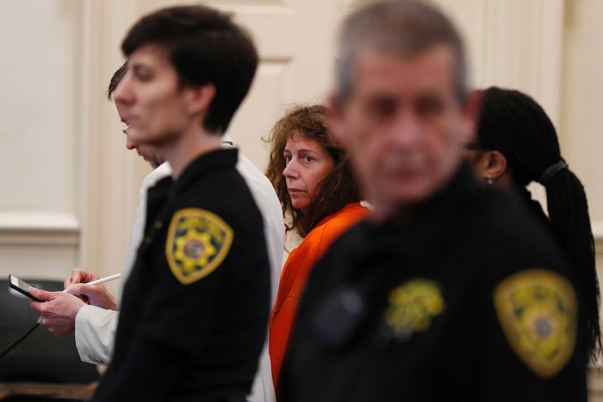 Carol Sharrow, dressed in orange, is flanked by security guards in court