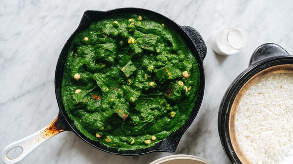 A cast-iron pan filled with spinach and chickpea curry next to a bowl of rice.