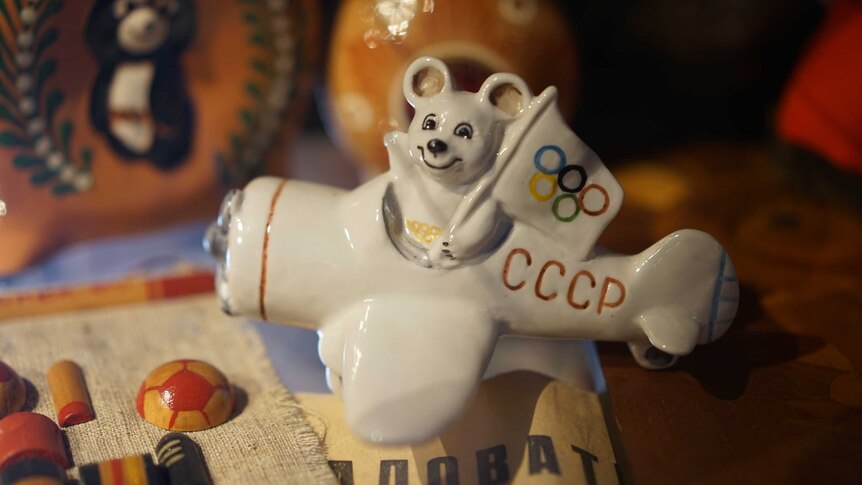 A ceramic model shows a bear holding an Olympic flag while sitting in a plane