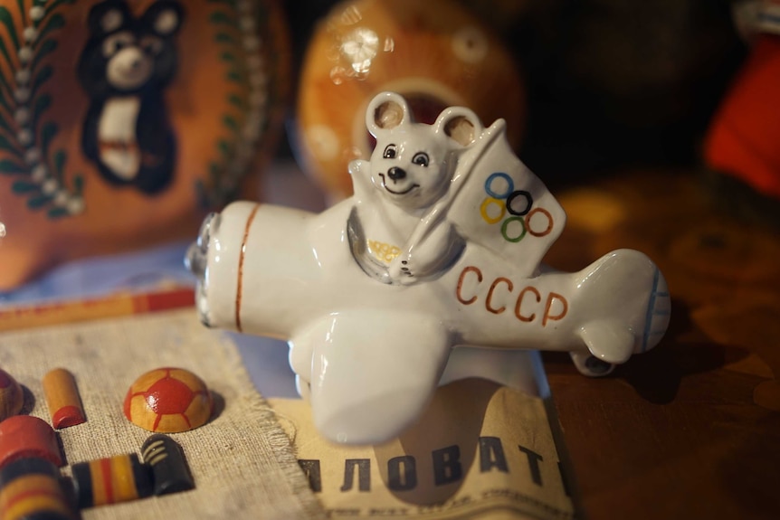 A ceramic model shows a bear holding an Olympic flag while sitting in a plane