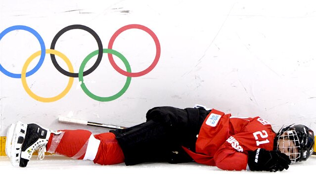 An ice hockey player lies injured on the rink in front of the Olympic rings.