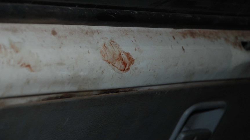 A close-up of the inside of a van shows red blood stains.