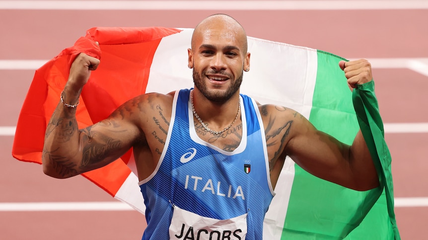 A man wearing a blue singlet holding a red, white and green flag in the air