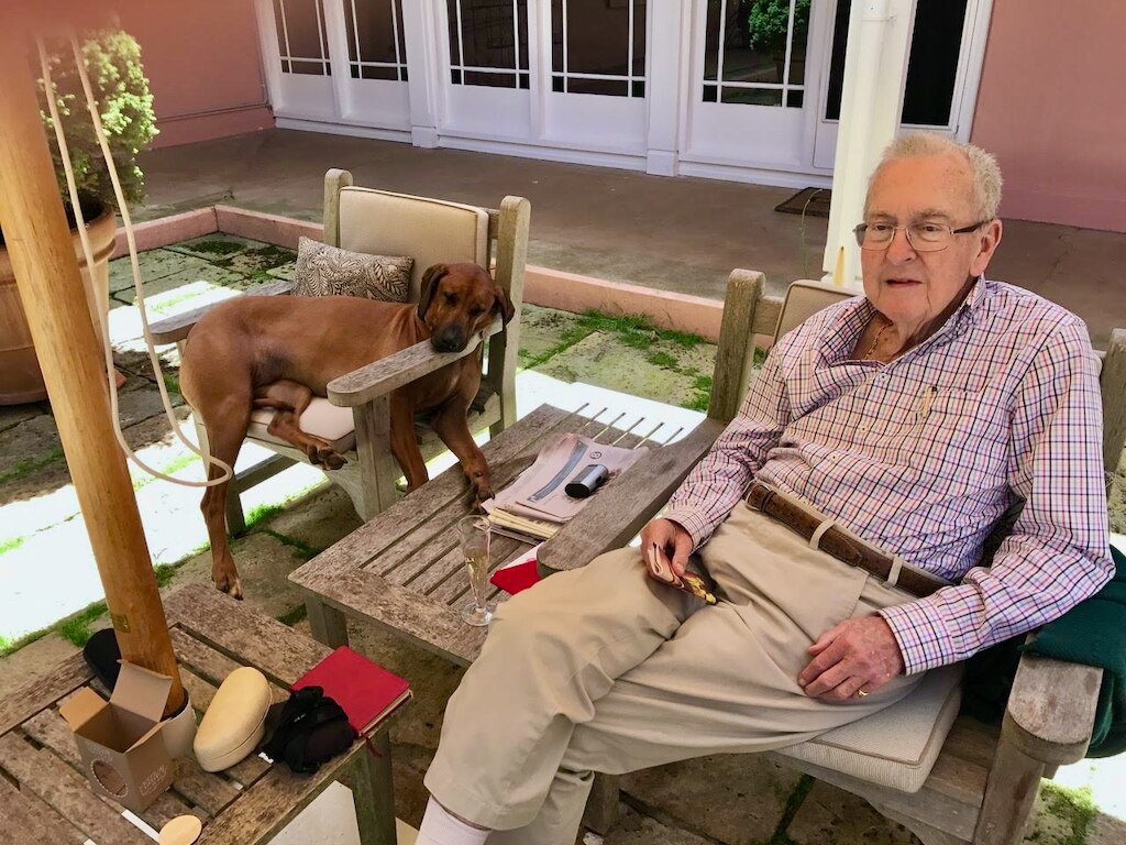 Elderly man sitting in a wooden outdoor seat in front of a pink and white building
